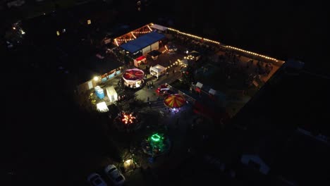 Illuminated-Christmas-funfair-festival-in-neighbourhood-pub-car-park-at-night-aerial-view