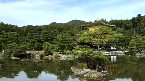 Templo-Kinkakuji-Rodeado-Por-Un-Tranquilo-Lago-Estanque-Con-árboles-De-Paisaje-Forestal-En-El-Fondo-En-Kyoto