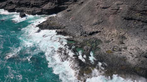 Perilous-beauty-unfolds-on-Hawaii's-coast,-with-towering-white-waves-and-distinctive-volcanic-rock