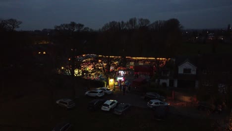 Illuminated-Christmas-fairground-festival-in-neighbourhood-car-park-at-night-aerial-rising-view