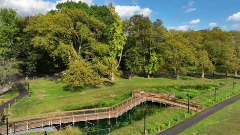 Park-with-a-wooden-footbridge,-winding-path,-and-lush-trees