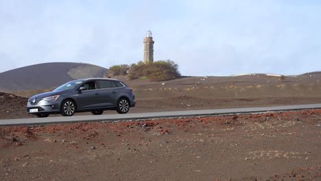 Car-stopped-with-warning-lights-in-Capelinhos-volcanic-landscape-with-lighthouse-in-background,-handheld