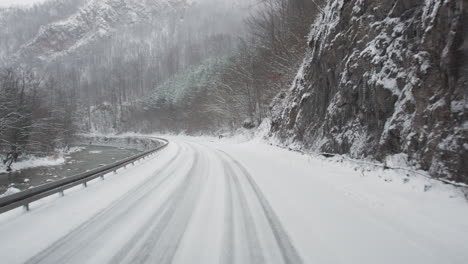 Fahren-Entlang-Eines-Flusses-Auf-Einer-Gefährlichen,-Vereisten-Canyon-Straße-Mit-Starkem-Schneefall