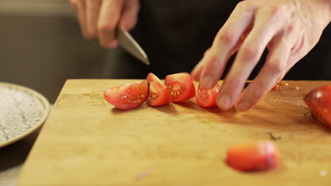 Chef-carefully-cuts-a-tomato-with-a-knife-on-a-wooden-board-using-clean-hands,-demonstrating-precision-and-hygiene