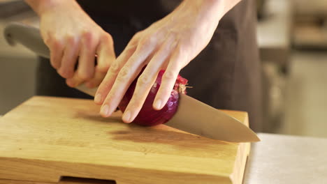 Chef-cuts-an-onion-with-a-knife-on-a-wooden-board-using-clean-hands,-demonstrating-precision-and-hygiene