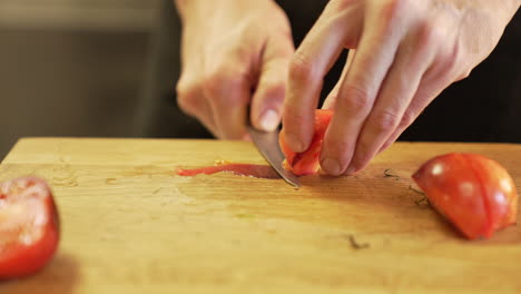 Chef-carefully-slices-a-tomato-peel-with-a-knife-on-a-wooden-board-using-clean-hands,-demonstrating-precision-and-hygiene