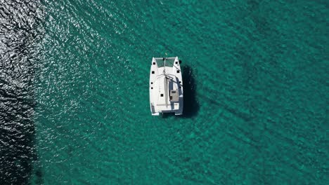 Barco-Catamarán-Con-Brillo-Solar-En-Aguas-Cristalinas-De-Color-Turquesa,-Aéreo