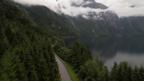 Vista-Aérea-De-La-Carretera-A-Lo-Largo-Del-Lago-Eikesdalsvatnet-En-Noruega-Con-Paisajes-Naturales-Montañosos-Y-Nubes-Bajas