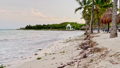 Nach-Links-Gleitende-Aufnahme-Eines-Wunderschönen-Strandes-In-Tulum-In-Der-Nähe-Von-Cancun,-Mexiko,-Mit-Kleinen-Wellen,-Palmen,-Blauem-Himmel-Und-Einigen-Wolken