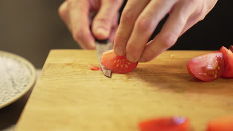 Chef-carefully-peels-a-tomato-with-a-knife-on-a-wooden-board-using-clean-hands,-demonstrating-precision-and-hygiene