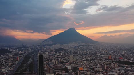 Impresionante-Puesta-De-Sol-Roja-Detrás-De-Una-Alta-Montaña-Y-El-Entorno-Urbano-De-Monterrey,-Nuevo-León,-México-En-Primer-Plano