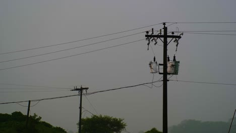 Silhouette-of-electricity-poles-and-wires-against-a-hazy-sky,-hinting-at-infrastructure