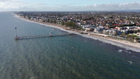 Rising-aerial-reveal-of-Brighton-beach-jetty-and-Adelaide-suburbs,-South-Australia
