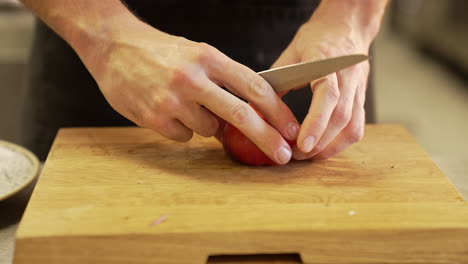 Chef-carefully-peels-a-tomato-with-a-knife-on-a-wooden-board-using-clean-hands,-demonstrating-precision-and-hygiene