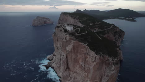 Cape-Caccia,-Sardinia:-aerial-view-approaching-the-lighthouse-of-this-famous-cape-on-the-island-of-Sardinia-and-during-sunset