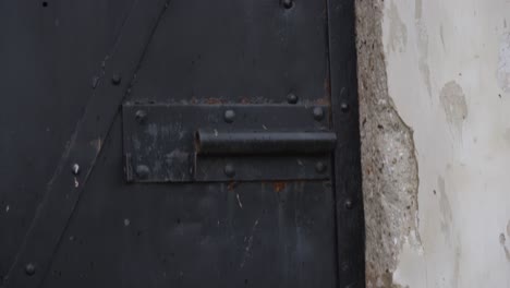 The-slow-motion-of-the-camera-reveals-an-old-rusty-worn-lock-on-a-black-metal-door-set-into-an-old-scratched-wall