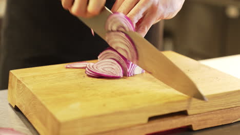 Chef-carefully-chops-an-onion-with-a-knife-on-a-wooden-board-using-clean-hands,-demonstrating-precision-and-hygiene