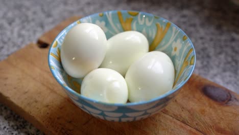 Hard-Boiled-Egg-In-A-Colorful-Bowl-Over-A-Wooden-Chopping-Board