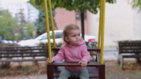 Little-girl-with-serious-look-on-face-being-pushed-on-swing-by-her-dad