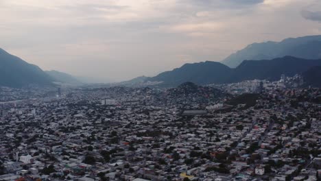 Wide-aerial-view-of-Monterrey,-Mexico-and-buildings-packed-into-the-valley-between-steep-mountains