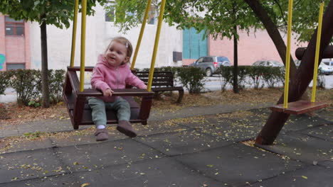 Cute-toddler-swinging-on-wooden-swing-in-city-park