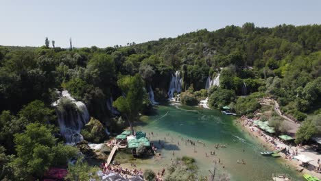 Drone-flyover-Crowded-tourist-area-of-Kravica-waterfall,-Scenic-landscape-in-Bosnia-and-Herzegovina