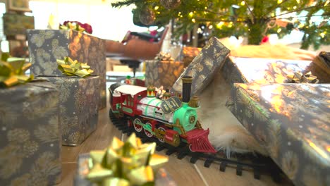 "Captivating-stock-footage:-Glide-beneath-a-festive-Christmas-tree,-presents-galore,-showcasing-a-model-train,-spreading-joy-in-a-delightful-forward-sliding-shot