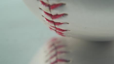 Cinematic-macro-shot-of-a-white-base-ball,-close-up-on-red-stitches,-baseball-on-a-mirror-reflecting-shiny-stand,-professional-studio-light,-4K-video-tilt-up