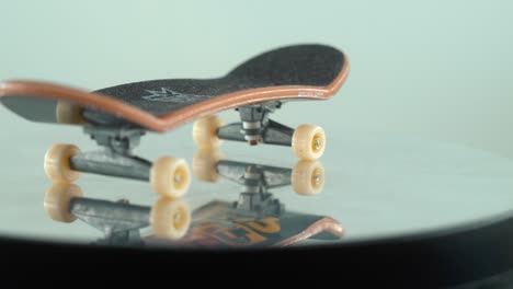A-detailed-close-up-shot-of-a-mini-skateboard,-tiny-white-wheels,-fingerboard-on-a-360-rotating-stand,-shiny-mirror-reflection,-professional-lighting,-cinematic-4K-video-pan-right