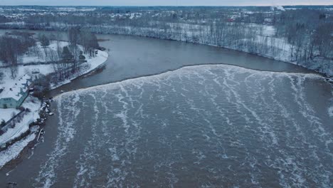 Aerial-establishing-view-of-Venta-river-rapids-during-winter-flood,-old-red-brick-bridge,-Kuldiga,-Latvia,-overcast-winter-day,-wide-drone-shot-moving-backward