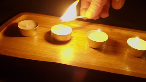 Hand-with-wooden-match-lights-tea-candles-in-decorative-wood-tray