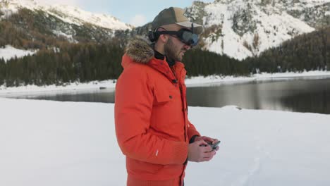 Drone-pilot-with-FPV-viewer-controlling-DJI-Avata-quadcopter-with-wireless-remote-control-surrounded-by-beautiful-mountains-and-snowy-landscape
