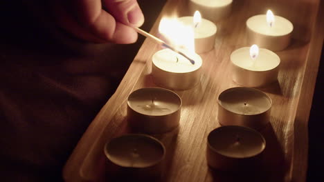 Man-lights-tea-candles-in-dark-studio,-flames-flicker-in-wooden-tray