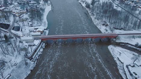 Aerial-establishing-view-of-Venta-river-rapids-during-winter-flood,-old-red-brick-bridge,-Kuldiga,-Latvia,-overcast-winter-day,-wide-drone-shot-moving-forward-tilt-down