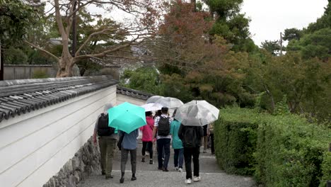 Touristen-Mit-Regenschirmen,-Die-Den-Weg-Auf-Dem-Byodo-in-Tempelgelände-In-Uji,-Japan,-Entlanggehen