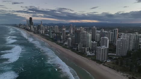 Gold-Coast,-Surfers-Paradise,-Queensland,-Australia,-drone,-Surf-breaking-on-the-colourful-sands-lit-by-sunset-skies