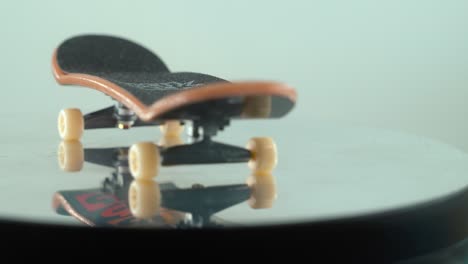 A-detailed-close-up-follow-shot-of-a-mini-skateboard,-tiny-white-wheels,-fingerboard-on-a-360-rotating-stand,-shiny-mirror-reflection,-professional-lighting,-cinematic-4K-video-pan-right