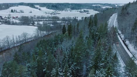 Aerial-establishing-view-of-valley-of-the-Abava-river-on-overcast-winter-day,-fields-covered-in-snow,-Abava-river-filled-with-dark-flood-water,-wide-drone-shot-moving-forward,-parallax-effect