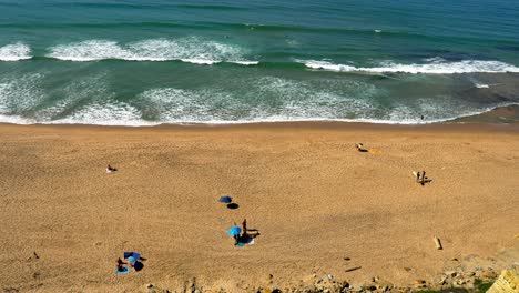 Portugal,-Carvoeira,-Foz-do-Lizandro-beach-with-sunbathing-people-and-surfers-in-the-Atlantic-Ocean