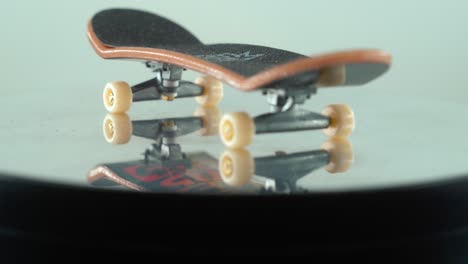 A-beautiful-detailed-close-up-shot-of-a-mini-skateboard,-tiny-white-wheels,-fingerboard-on-a-360-rotating-stand,-shiny-mirror-reflection,-professional-lighting,-cinematic-4K-video-tilt-down