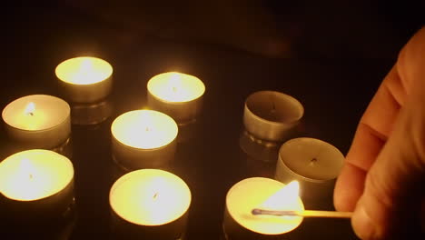 Camera-dolly-shot:-Tea-candles-are-lit-with-burning-match-in-dark-room
