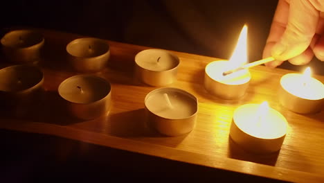 Man-lights-tea-candles-in-wooden-tray-in-dark-room-as-camera-dollies