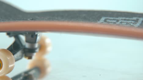 Eine-Makrodetaillierte-Folgeaufnahme-Eines-Mini-Skateboards,-Winzige-Weiße-Räder,-Griffbrett-Auf-Einem-Um-360-Grad-Drehbaren-Ständer,-Glänzende-Spiegelreflexion,-Professionelle-Beleuchtung,-Filmischer-4K-Videoschwenk-Nach-Rechts