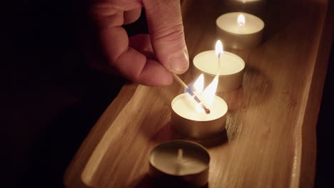 New-tea-candles-are-lit-with-wooden-match-flame-in-dark-room-tray