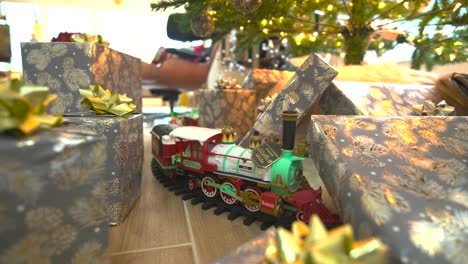 Captivating-stock-footage:-Glide-beneath-a-festive-Christmas-tree,-presents-galore,-showcasing-a-model-train,-spreading-joy-in-a-delightful-wide-reverse-sliding-shot
