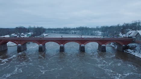 Aerial-establishing-view-of-Venta-river-rapids-during-winter-flood,-old-red-brick-bridge,-Kuldiga,-Latvia,-overcast-winter-day,-wide-drone-shot-moving-forward
