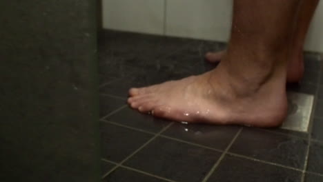 Low-angle-view-of-defocused-male-feet-in-shower,-focus-on-foreground