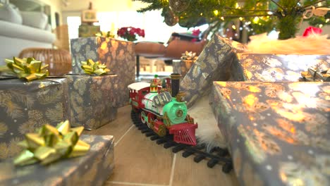 Glide-beneath-a-festive-Christmas-tree,-presents-galore,-showcasing-a-model-train,-spreading-joy-in-a-delightful-wide-forward-sliding-shot