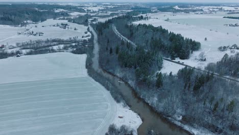 Luftaufnahme-Des-Tals-Des-Abava-Flusses-An-Einem-Bewölkten-Wintertag,-Schneebedeckte-Felder,-Mit-Dunklem-Hochwasser-Gefüllter-Abava-Fluss,-Weite-Drohnenaufnahme,-Die-Sich-Vorwärts-Bewegt