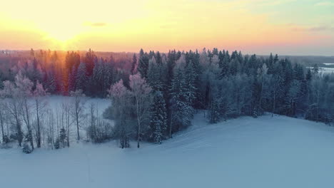 Aerial-tracking-shot-revealing-a-hut-and-a-sauna-at-a-forest-lake,-frosty-sunrise